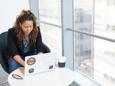 woman sits on padded chair while using MacBook during daytime